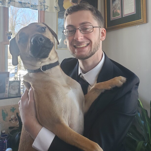 Chase wearing a suit and smiling while posing with his dog.