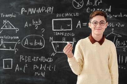 High school student standing in front of a chalkboard with geometry equations.